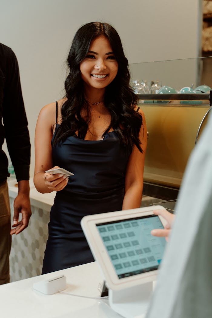 services-01 A woman in a black dress smiling while making a cashless payment at a store.